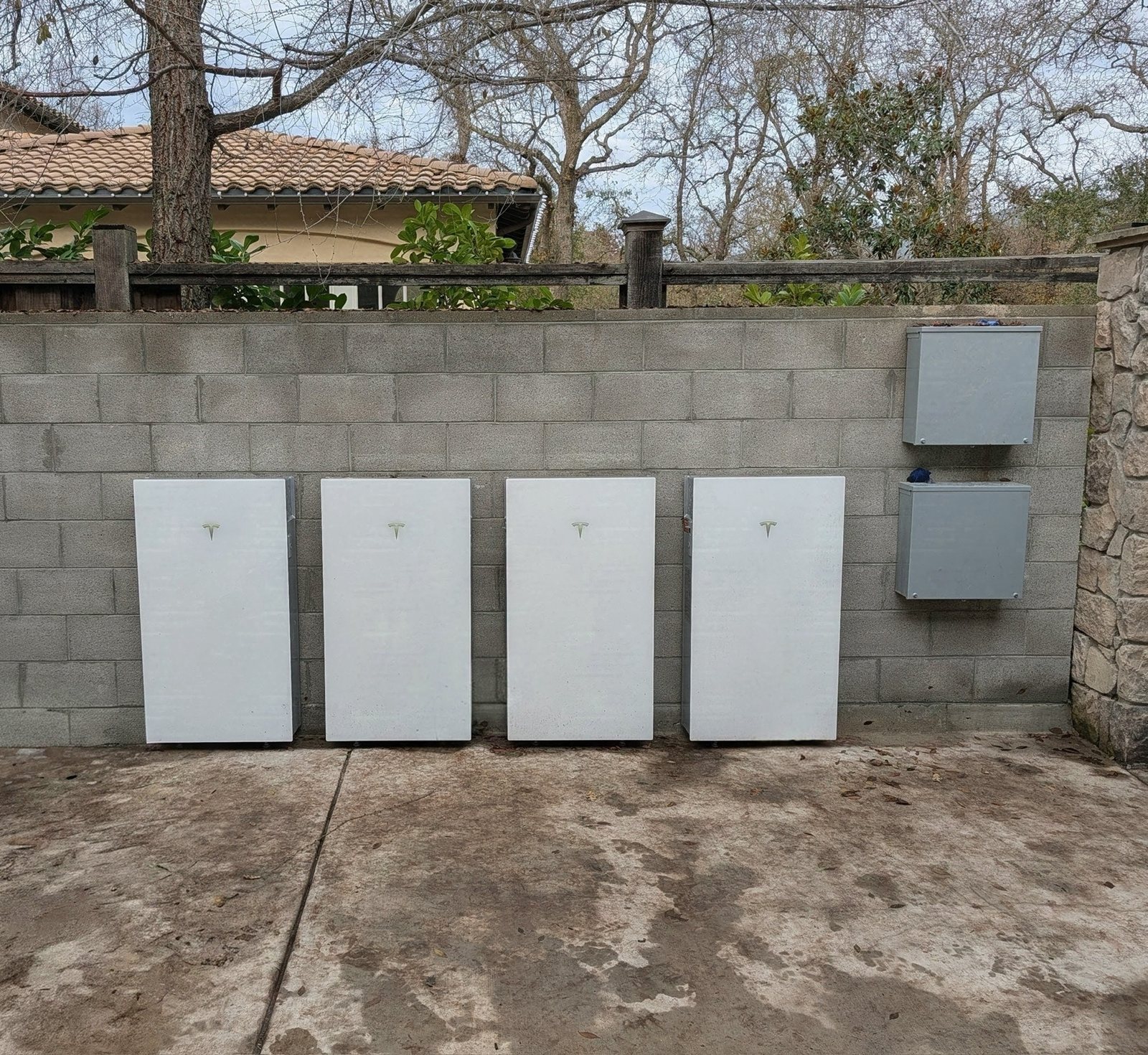 Four Tesla Powerwalls installed along a block wall